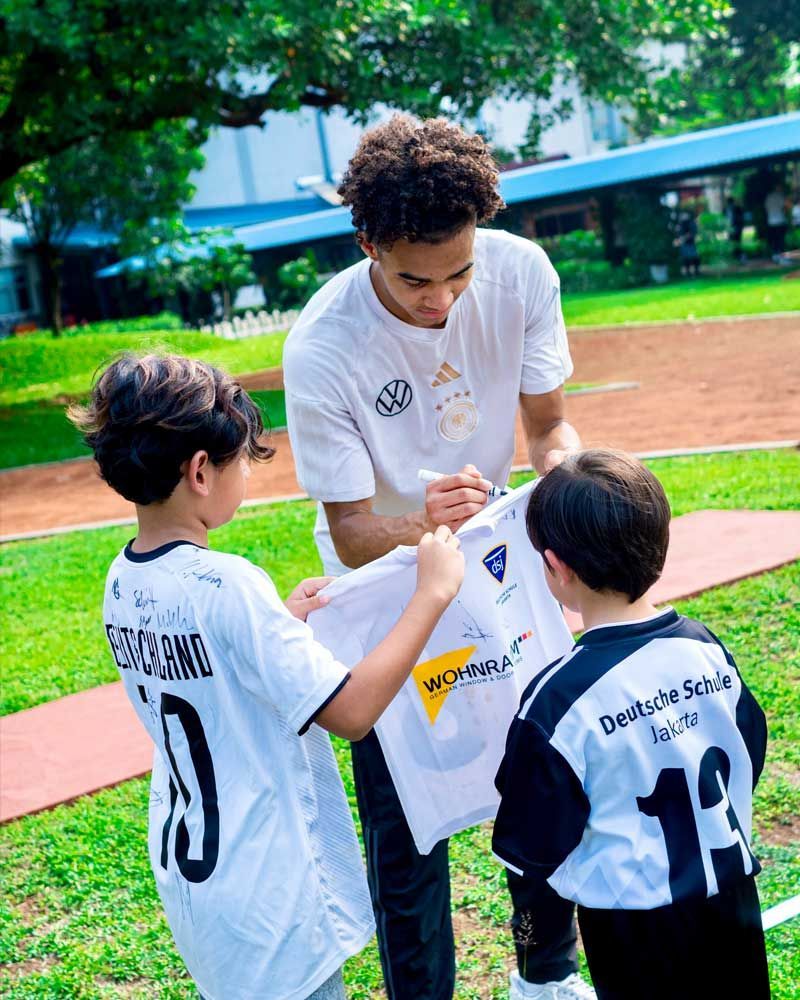 A man is signing a soccer jersey for two young boys.