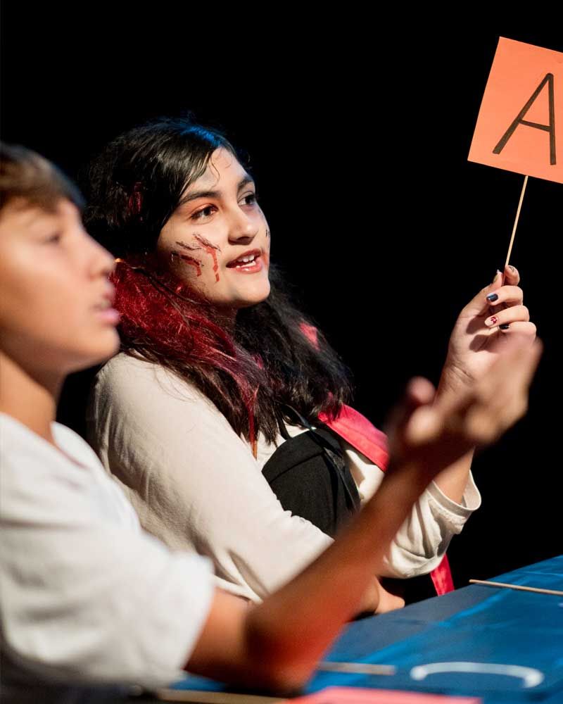 A boy and a girl are sitting at a table holding a sign that says a