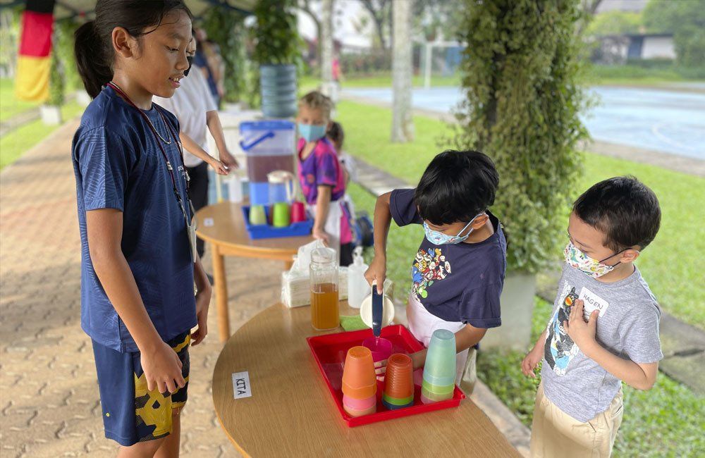A group of children are standing around a table playing with cups.