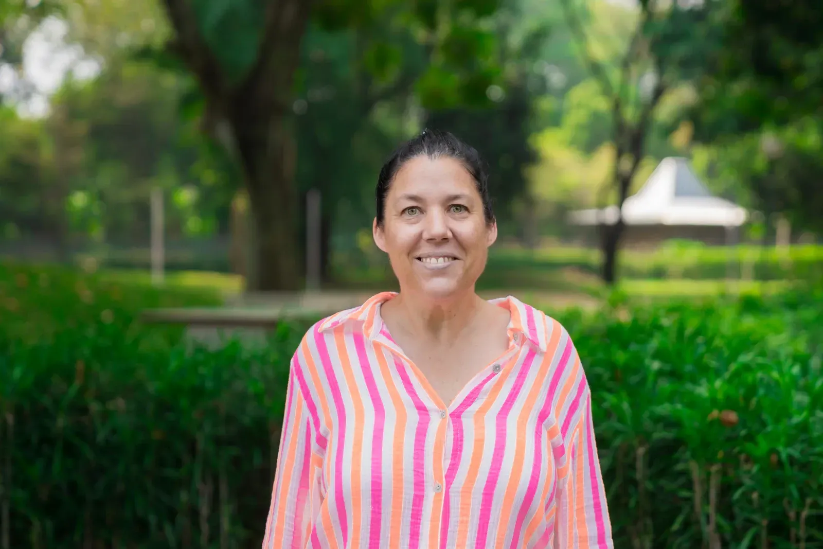 A woman in a brown shirt is smiling in front of a building.