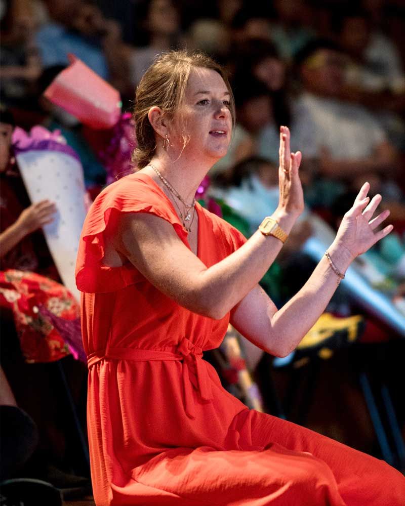 A woman in a red dress is clapping her hands in front of a crowd.