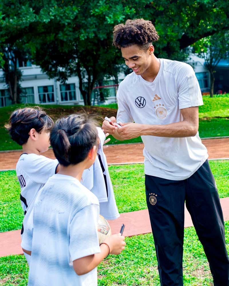 A man is talking to two young boys on a field.