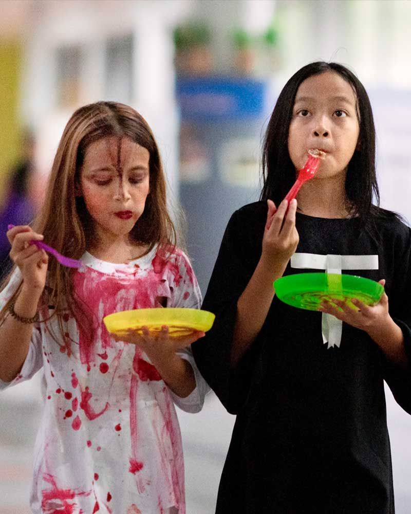 Two little girls are eating from plastic plates with spoons.