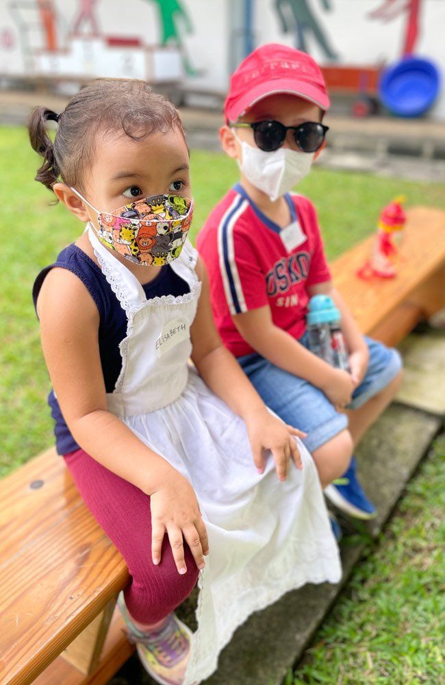 A boy and a girl wearing face masks are sitting on a bench.