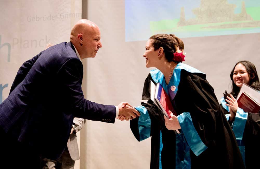 A man and a woman are shaking hands at a graduation ceremony.