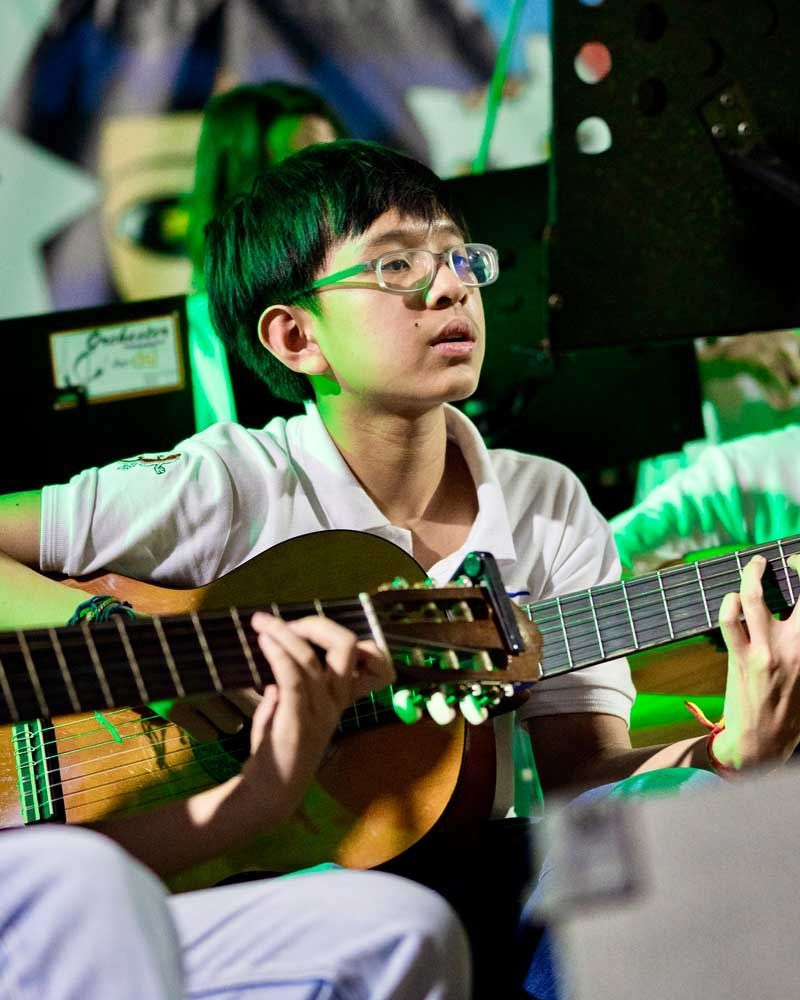 A young boy wearing glasses is playing a guitar