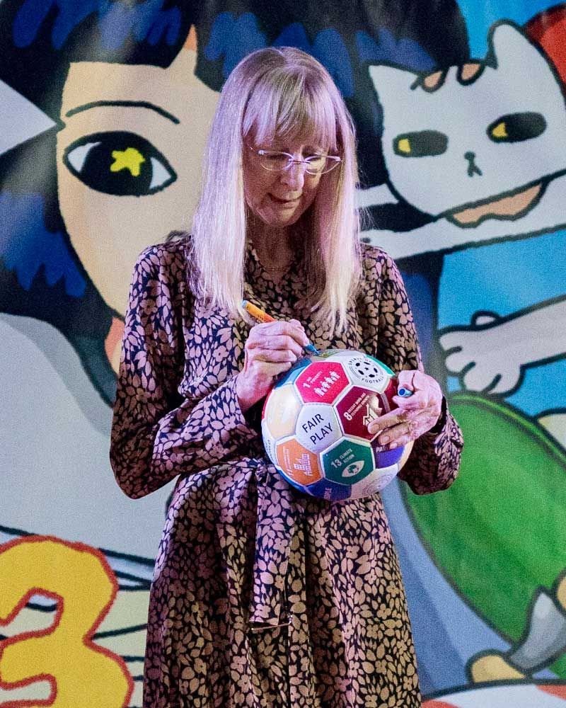 A woman is holding a soccer ball and writing on it