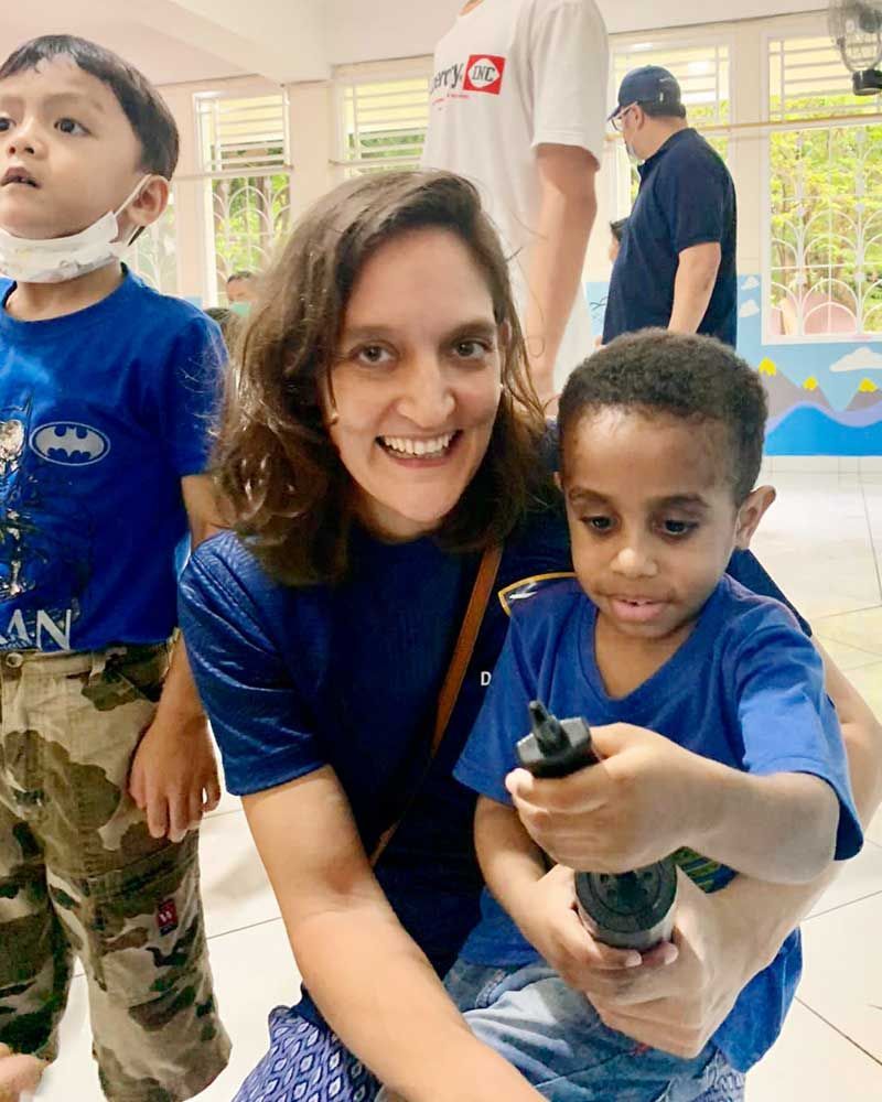 A smiling woman in a blue shirt poses with a young boy holding a small object during a donation day.