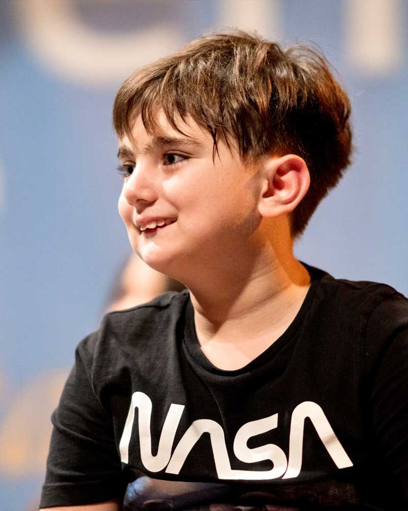 A smiling boy wearing a NASA t-shirt, enjoying a moment on stage.