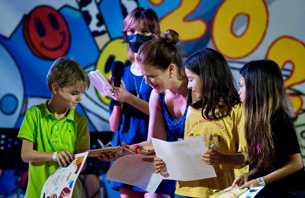 A group of children are standing in front of a wall with a smiley face on it.