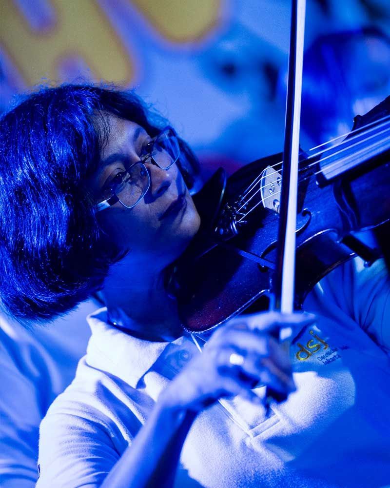 A woman with blue hair and glasses is playing a violin