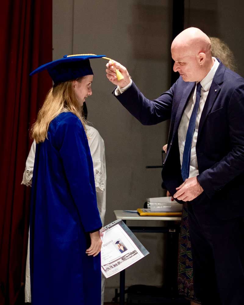 A man in a suit is giving a diploma to a woman in a graduation cap and gown.