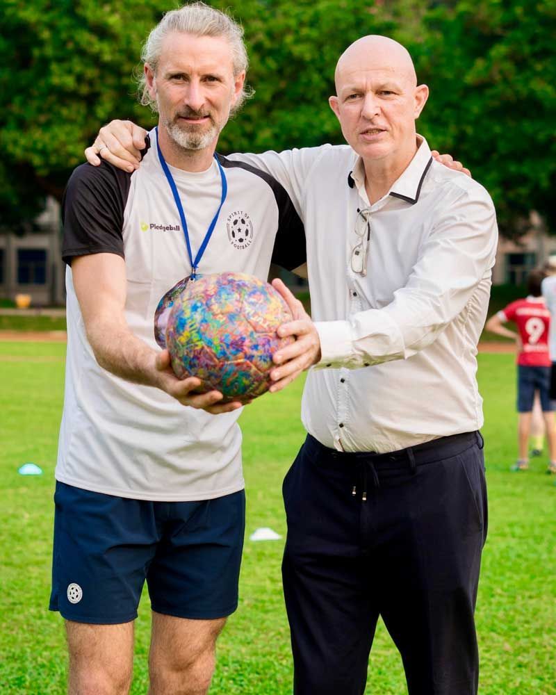 Two men are standing next to each other holding a soccer ball