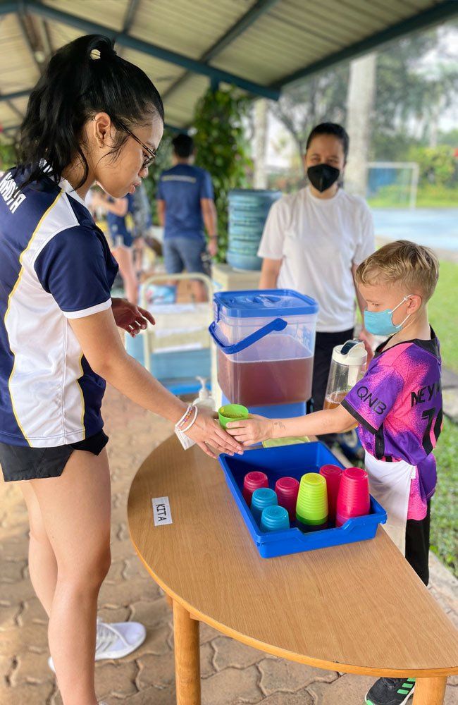A woman is standing next to a boy playing with cups at a table.