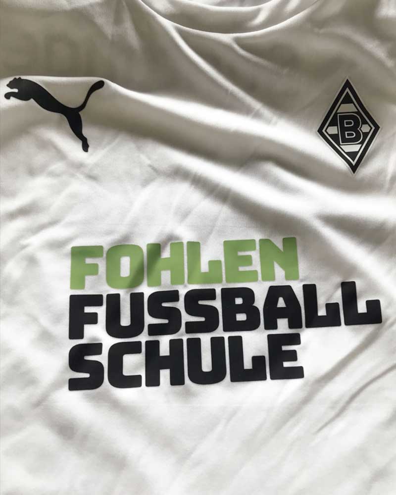 A white shirt with the words fohlen fussball schule on it