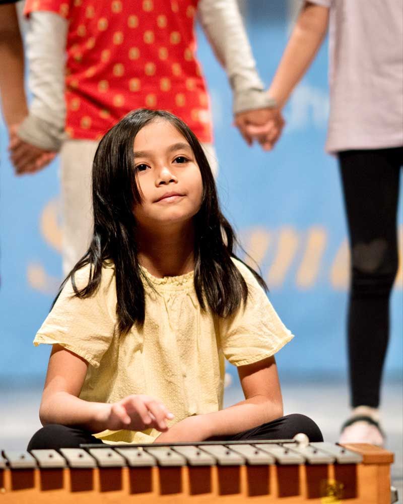 A young girl is sitting on the floor playing a xylophone.