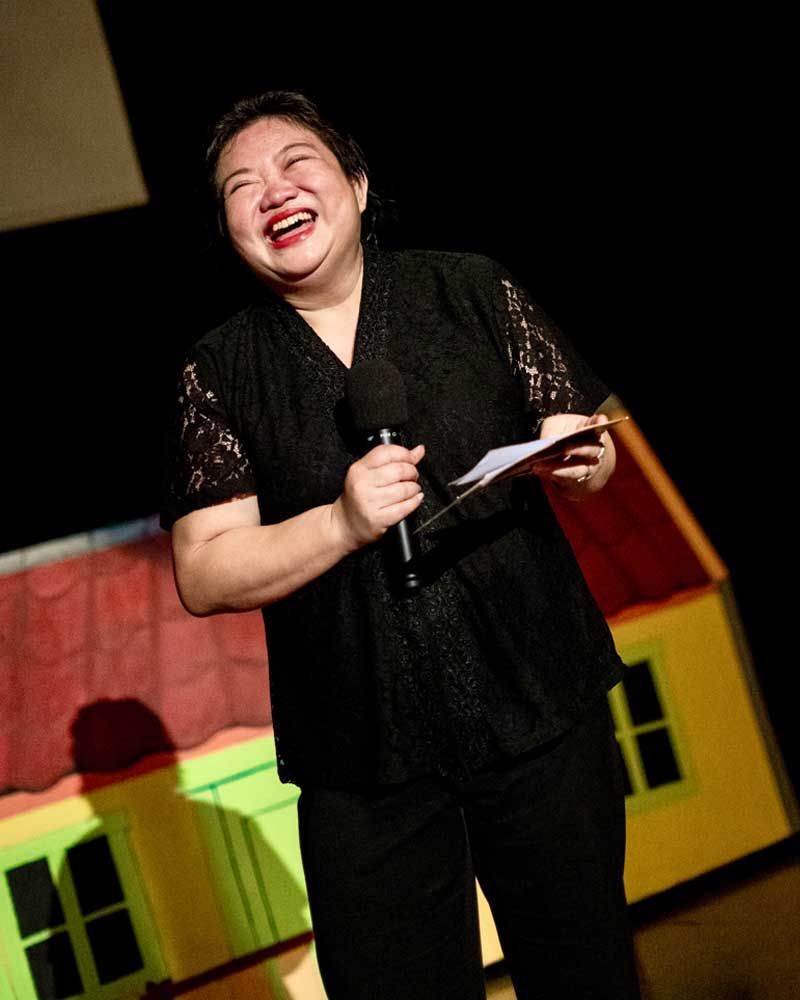 A woman in a black shirt is holding a microphone and smiling