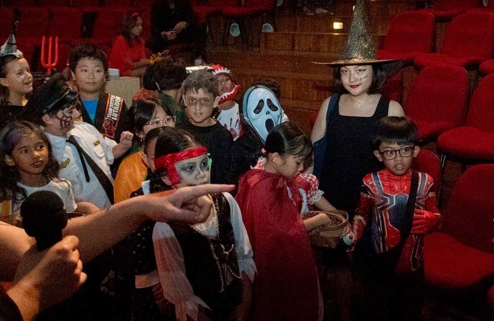 A group of children dressed in halloween costumes are standing in a theater.