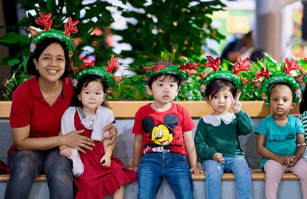 A group of children are sitting on a bench wearing christmas hats.
