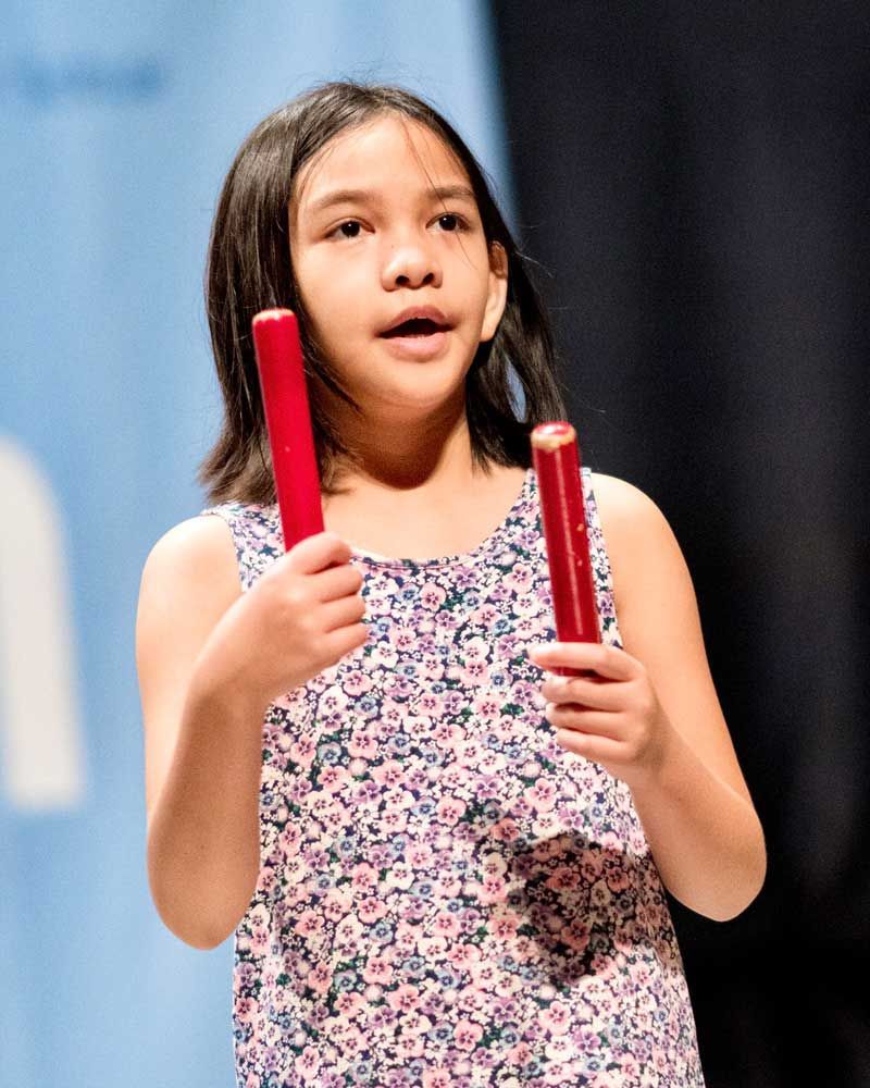 A little girl is holding two red sticks in her hands