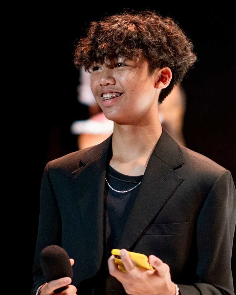 A young man in a suit is holding a cell phone and a microphone.