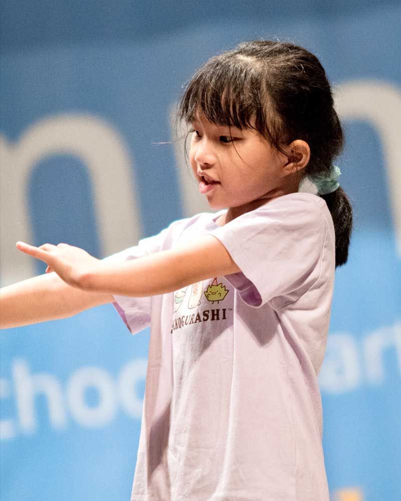 A little girl is wearing a purple t-shirt and pointing at something.
