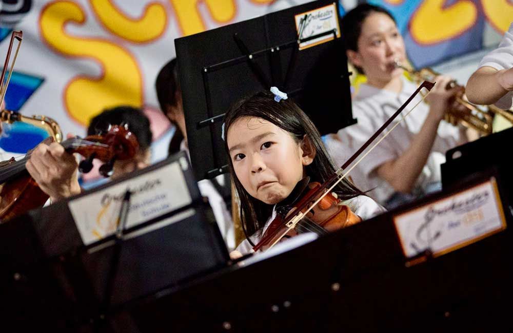 A young girl is playing a violin in an orchestra.