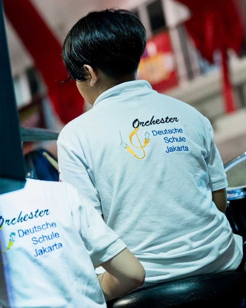 A boy wearing a white shirt that says orchester on it