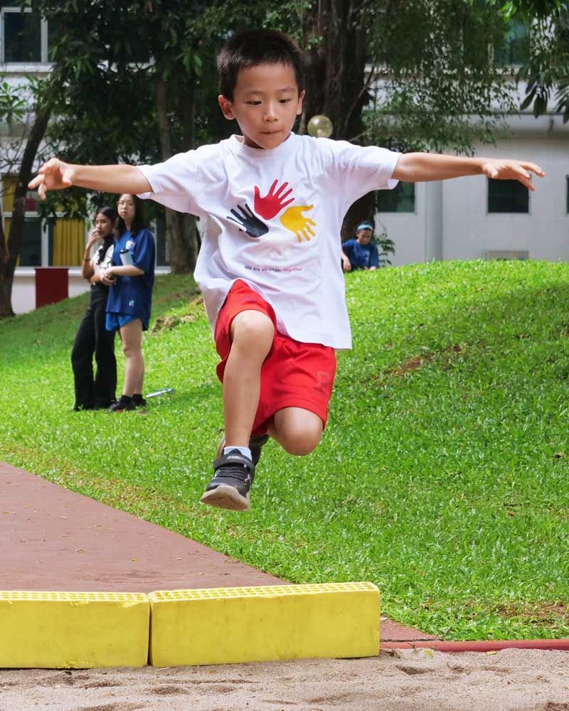 A young boy in a white shirt with hands on it is jumping in the air