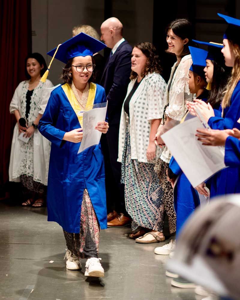 A girl in a blue graduation cap and gown is walking on stage