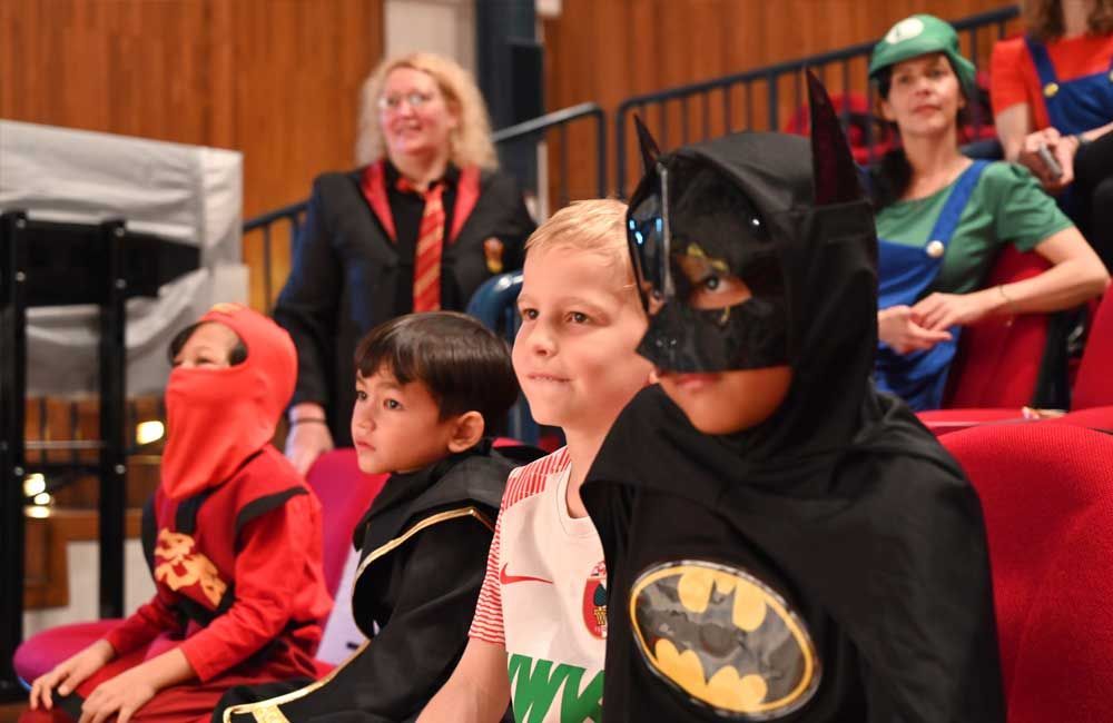 A group of children dressed in costumes are sitting in a theater.