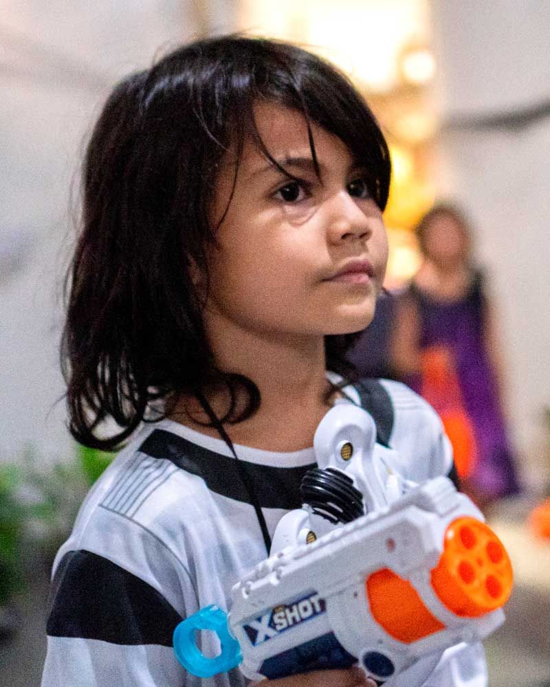 A child in a futuristic warrior costume holds a toy blaster, enjoying the Halloween festivities with decorations