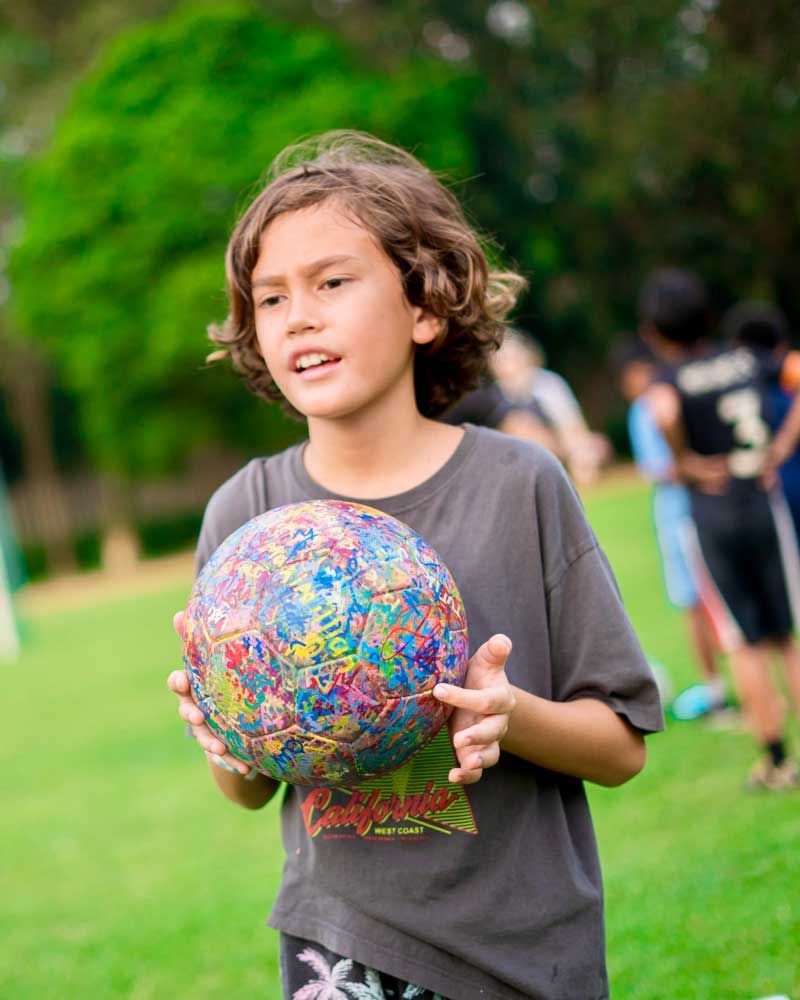 A young boy is holding a colorful soccer ball in a field.