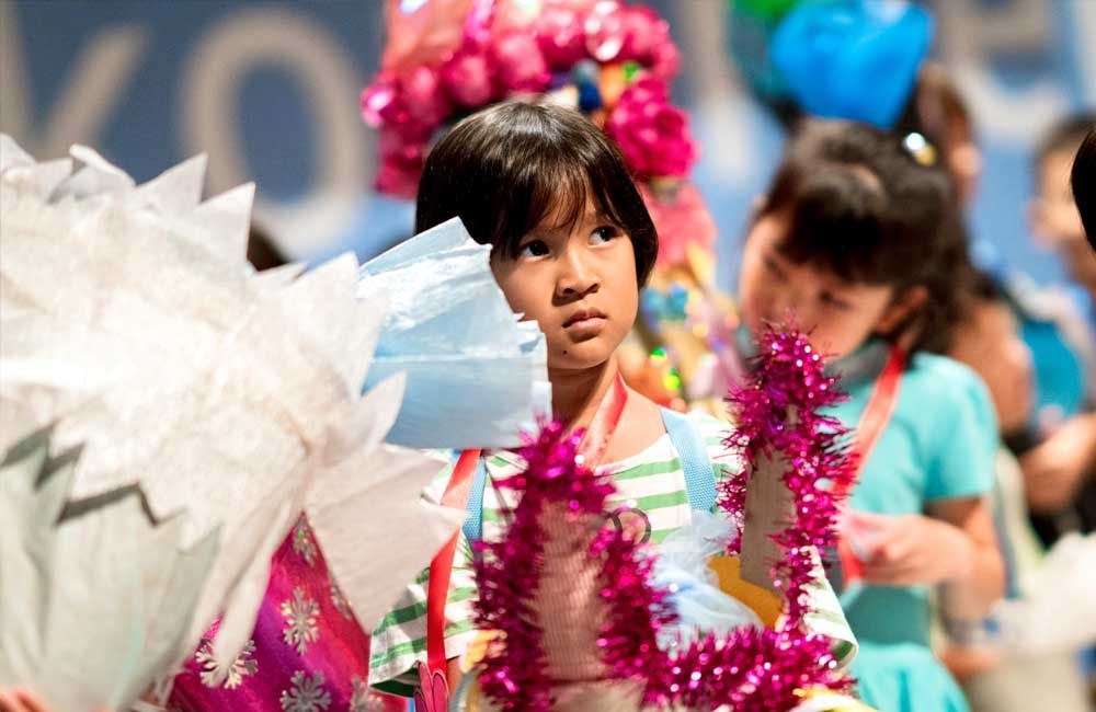 A little girl wearing a lei is standing in a crowd of children.