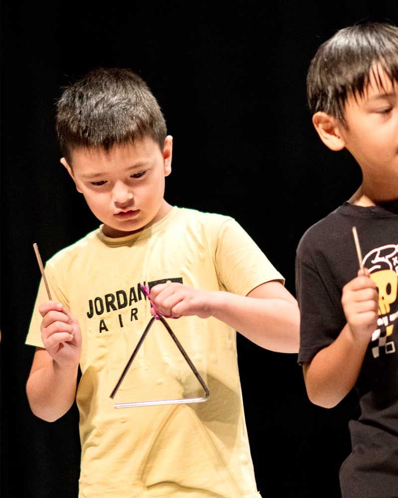 A boy wearing a jordan air shirt is playing a triangle