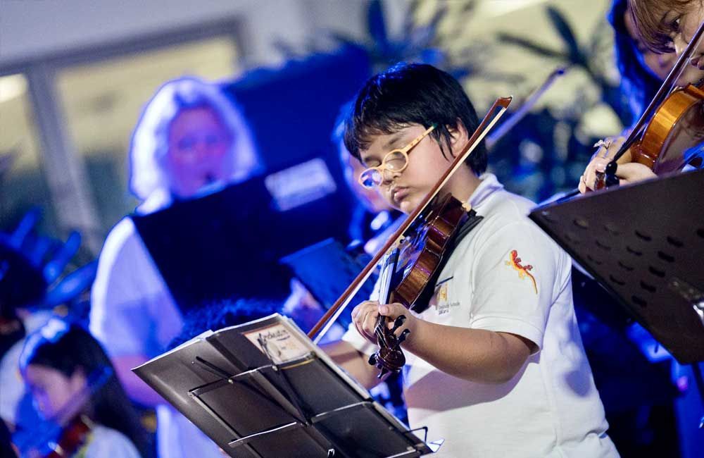 A young boy is playing a violin in an orchestra.