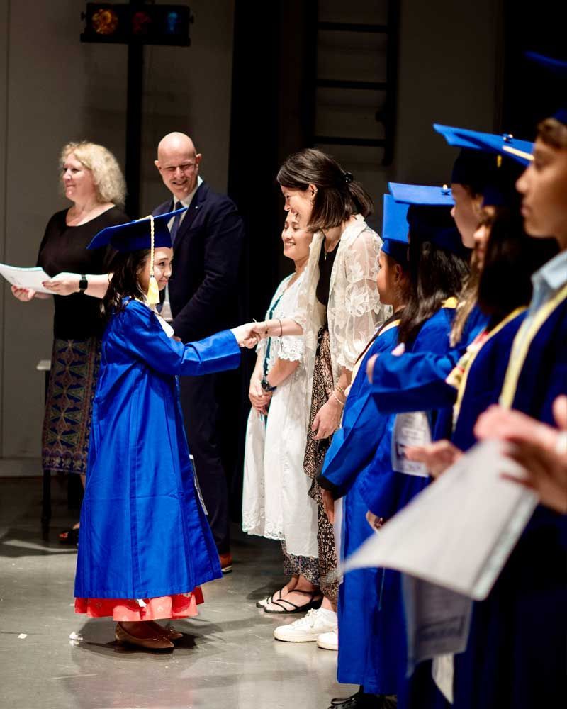 A girl in a blue cap and gown is standing in front of a group of people