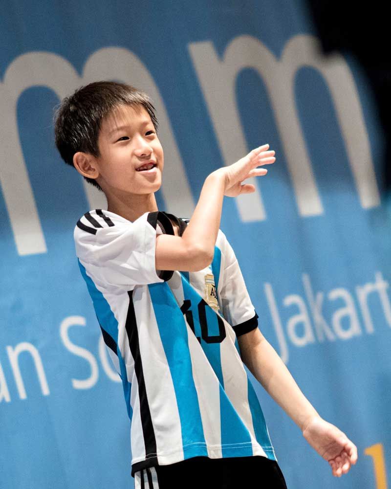 A young boy stands in front of a sign that says jakarta