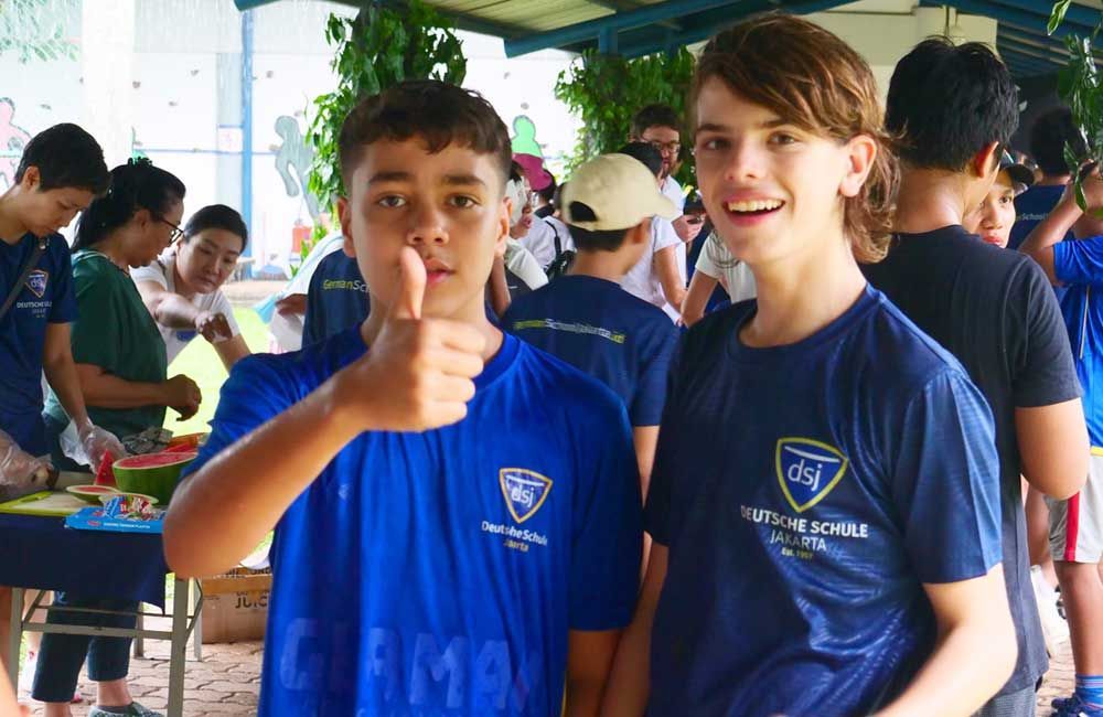 Two boys in blue shirts are giving a thumbs up