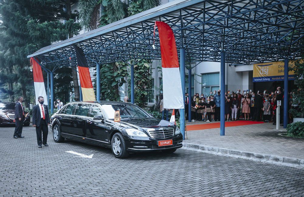 A black car is parked under a canopy in front of a building.