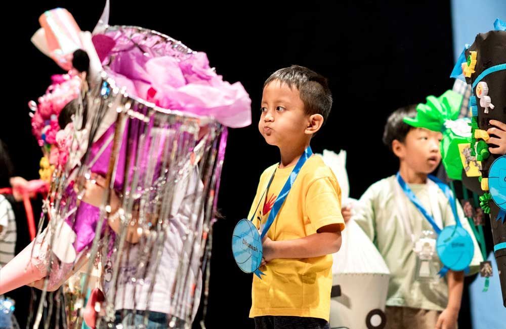 A boy in a yellow shirt is standing in front of a group of children.