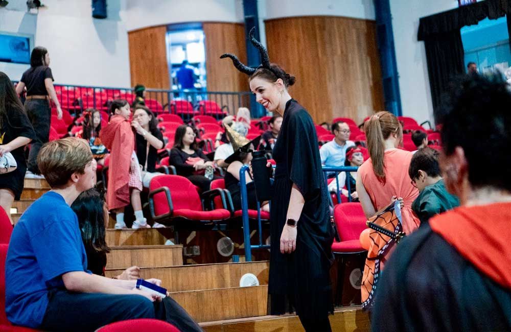A woman in a devil costume is standing in front of a crowd of people in an auditorium.