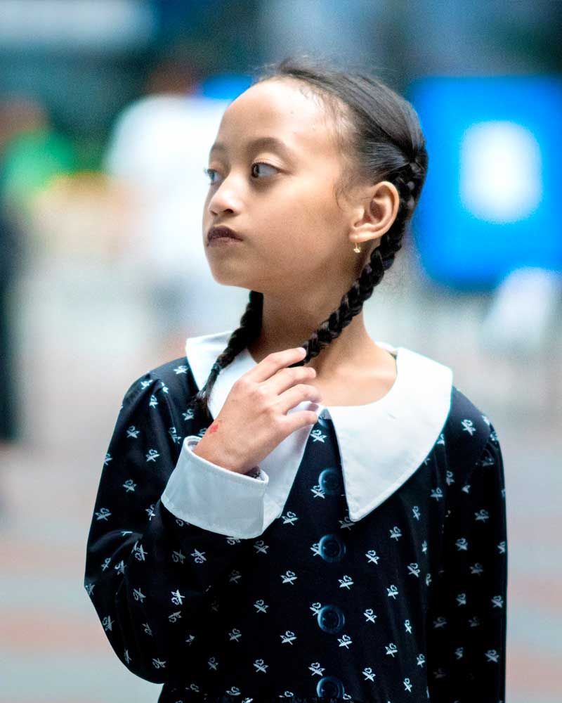 A little girl with braids is wearing a black dress and a white collar.