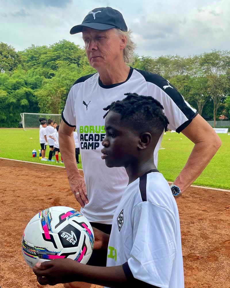 A man is standing next to a boy holding a soccer ball.