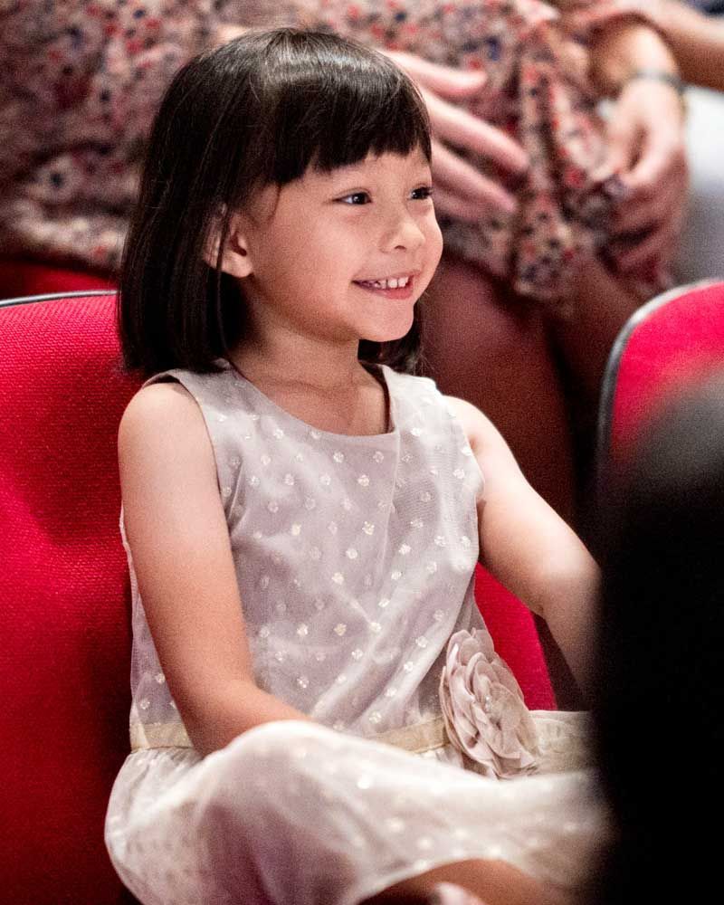 A little girl is sitting in a red chair and smiling.