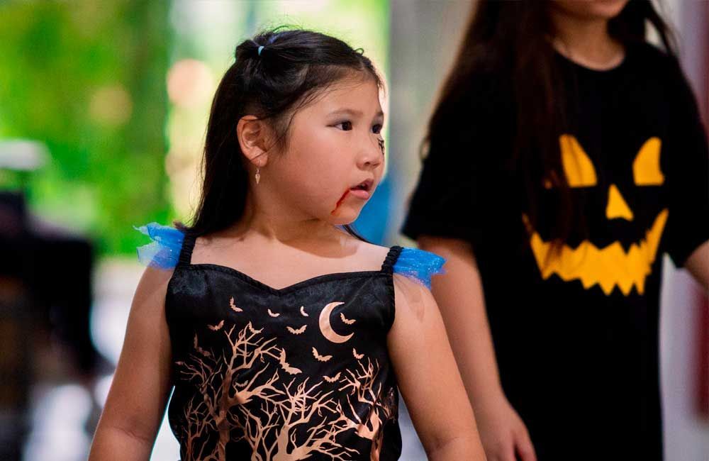 A little girl in a vampire costume is standing next to a little girl in a pumpkin shirt.
