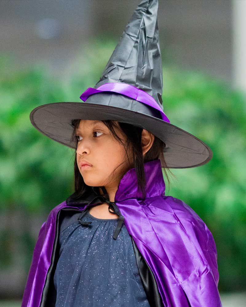 A little girl is wearing a witch hat and a purple cape.