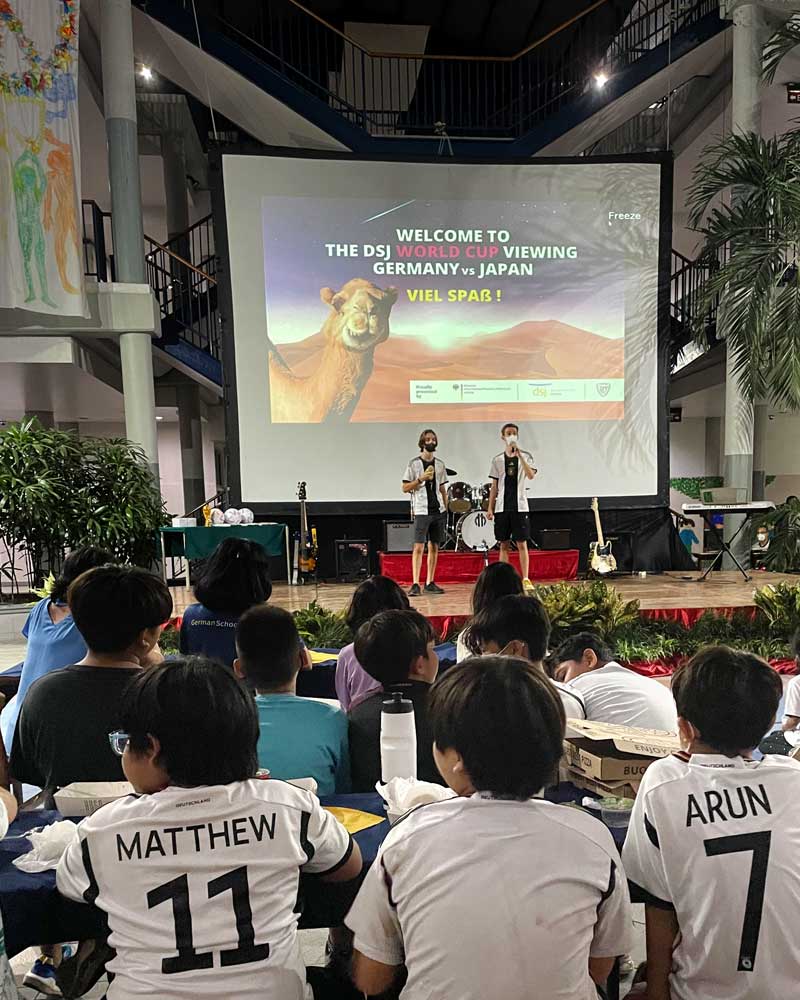 A group of children are sitting in front of a large screen watching a presentation.