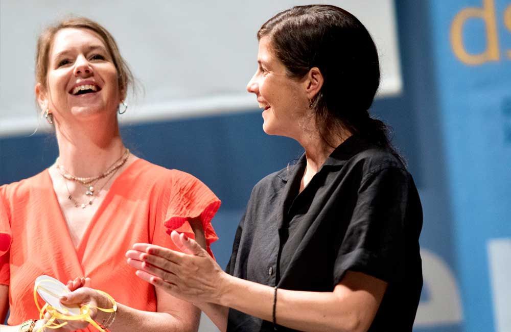 Two women are standing next to each other on a stage and laughing.