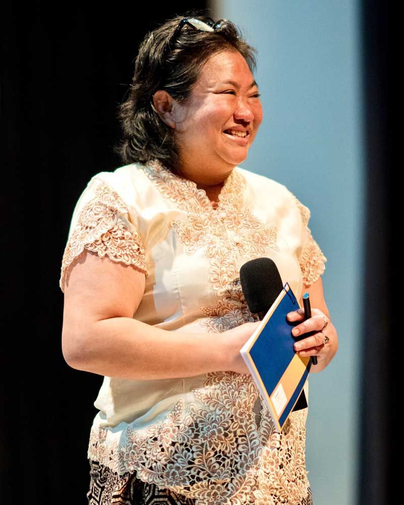 A woman is smiling while holding a microphone and a book